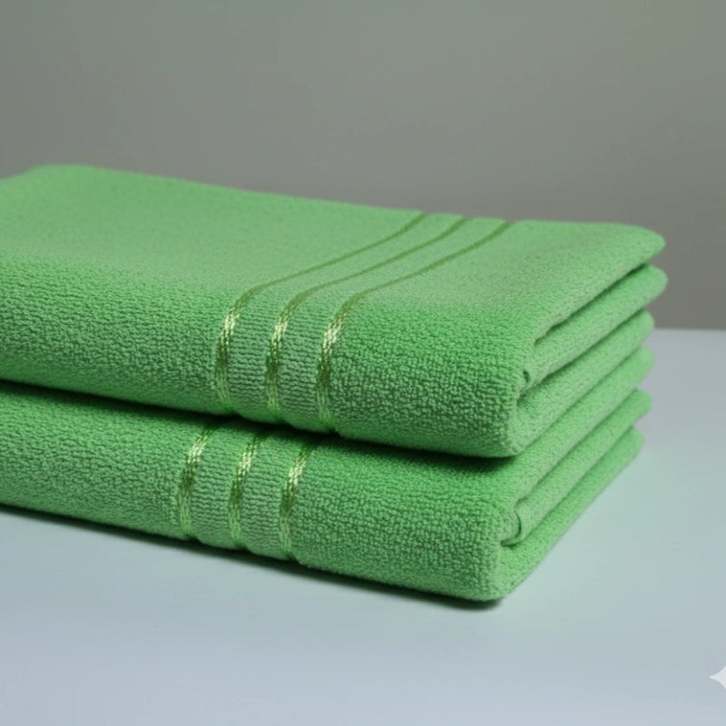 Two green towels stacked on a light gray surface with a neutral background