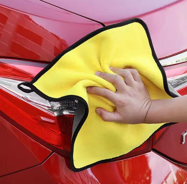 Person cleaning a red car with a yellow microfiber towel
