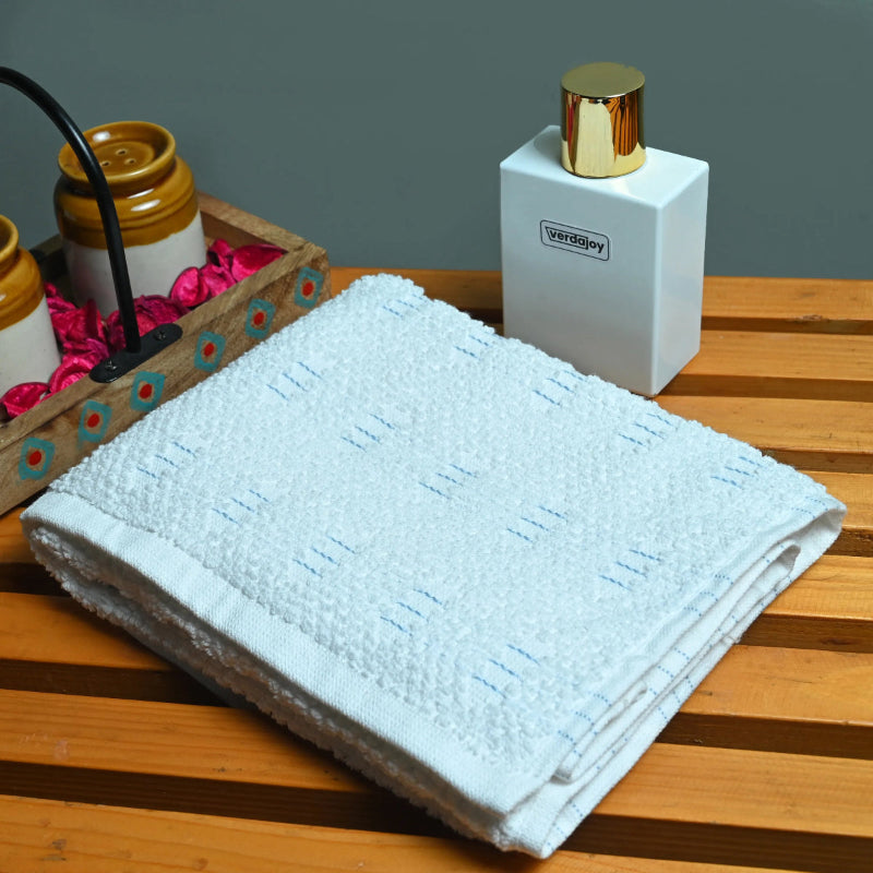 Folded light blue towel on a wooden surface with a white container and decorative items in the background.