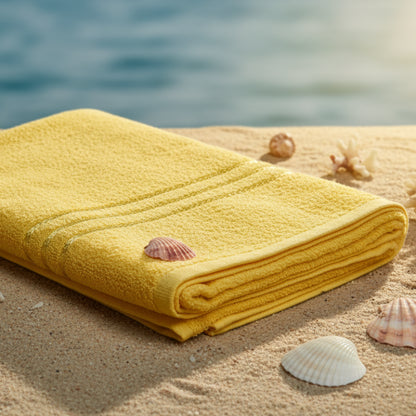Yellow towel on a beach surface with sea shell and ocean in background.