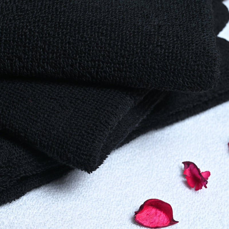 Stack of black towels on a white surface with pink petals and a butterfly.