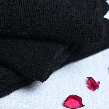 Stack of black towels on a white surface with pink petals and a butterfly.