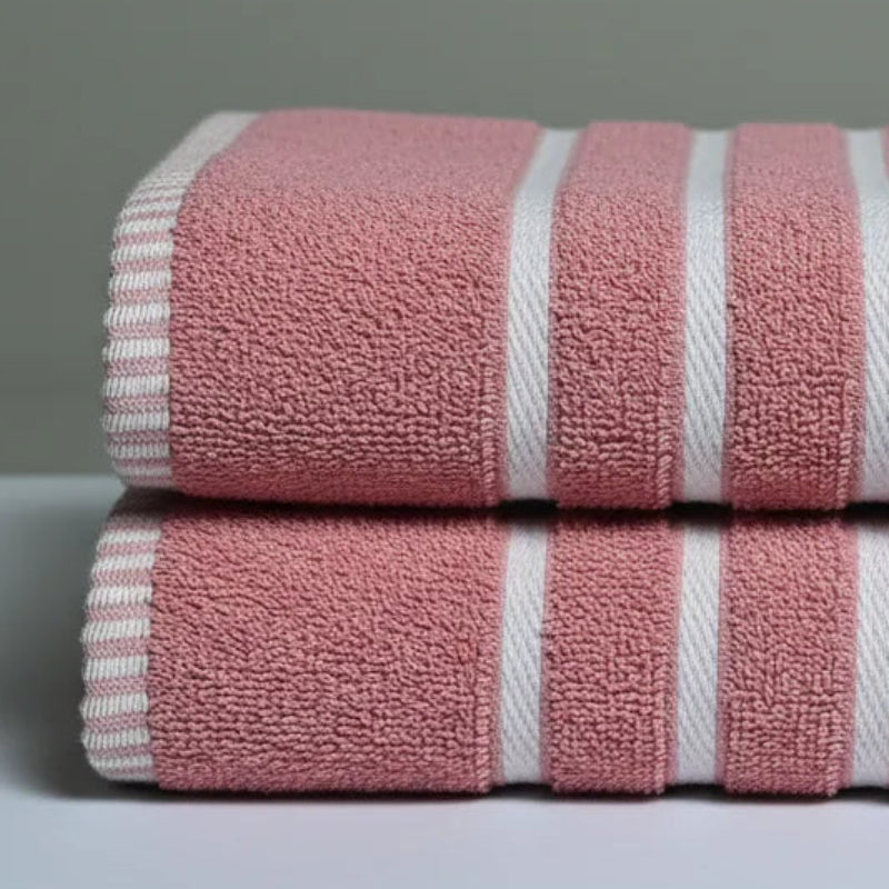 Two pink towels with white stripes stacked on a gray surface against a gray background