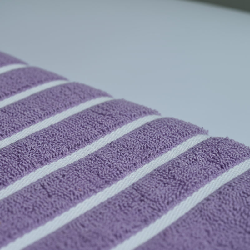 Fabric Closeup of purple bath towel with 4 strips of white color.