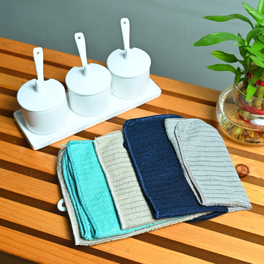 Set of colorful kitchen towels on a wooden table with white containers and a plant in the background.