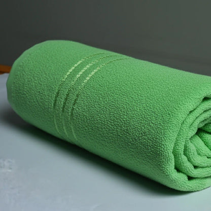 a green bath towel rolled on a white base and grey background