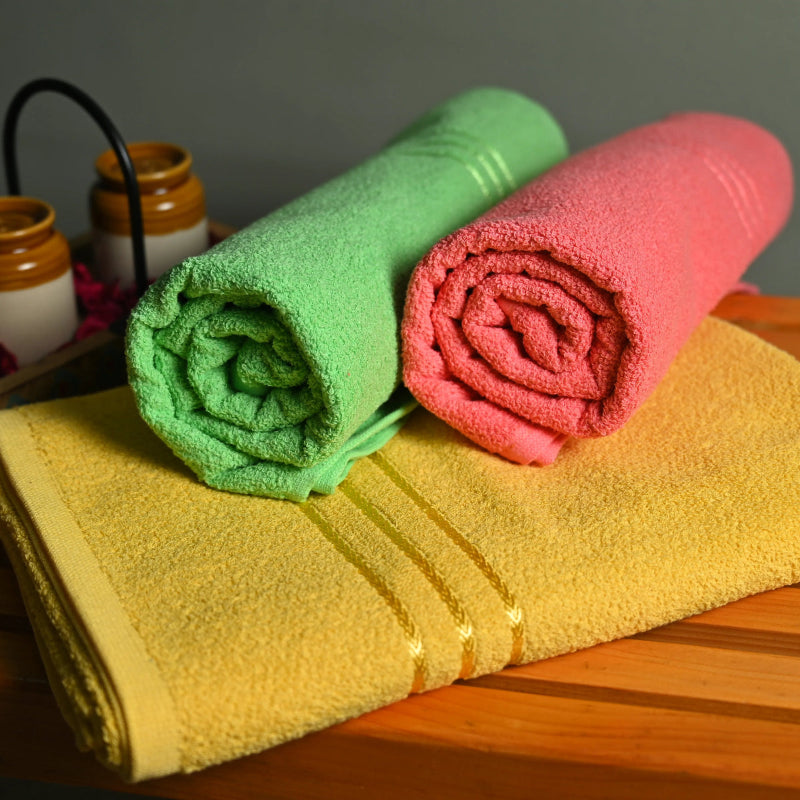Three folded towels in green, pink, and yellow on a wooden surface with a gray background.
