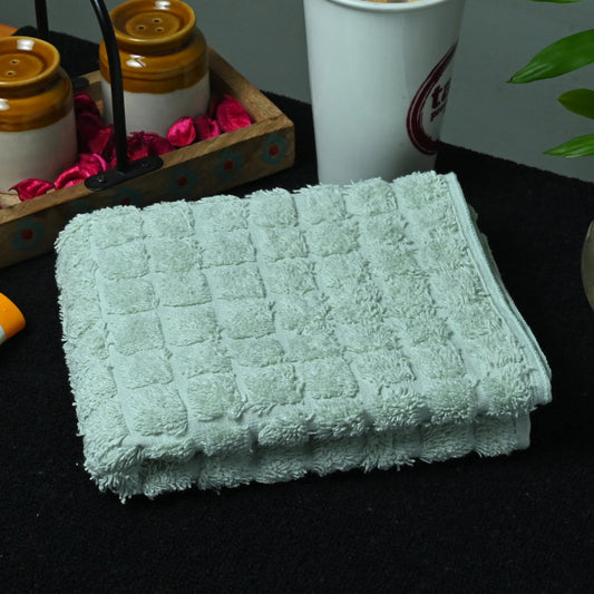 Stack of green towels on a dark surface with a cup, toothbrushes, and a plant in the background.