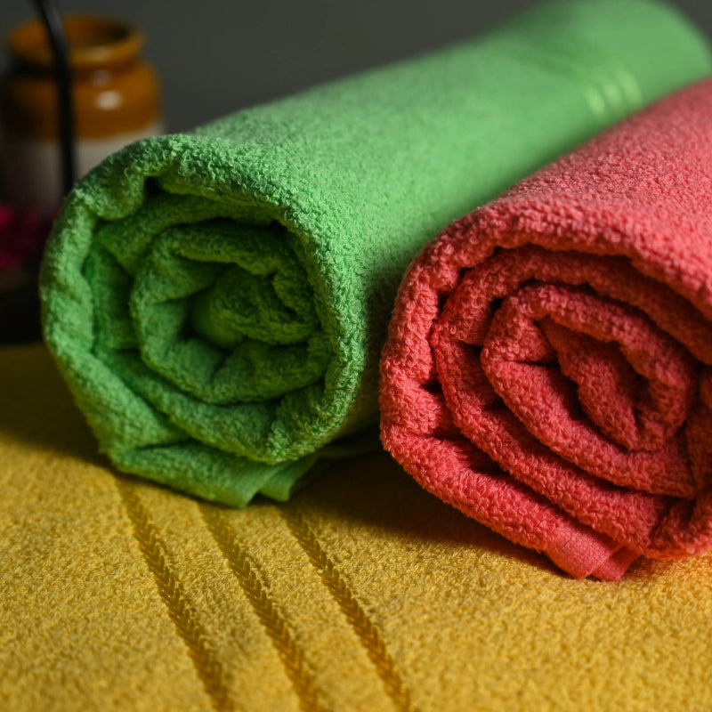 Two rolled-up towels, one green and one red, on a yellow surface with blurred jars in the background.