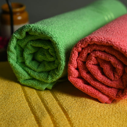 Two rolled-up towels, one green and one red, on a yellow surface with blurred jars in the background.