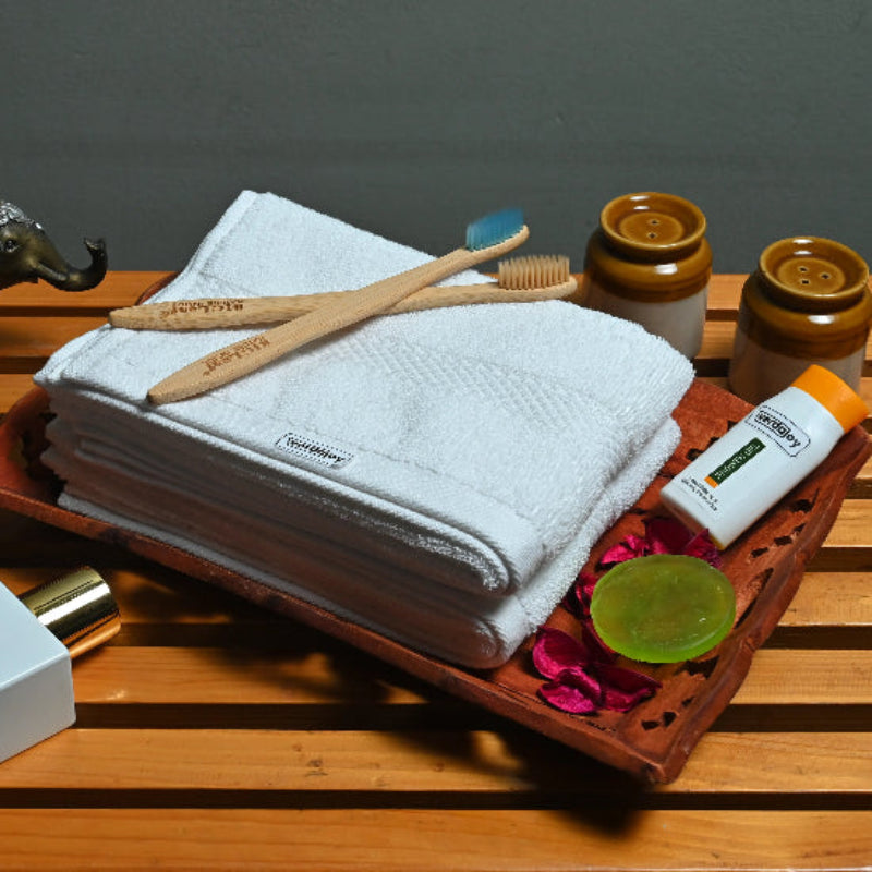Towel, bamboo toothbrush, and skincare products on a wooden tray with a dark background