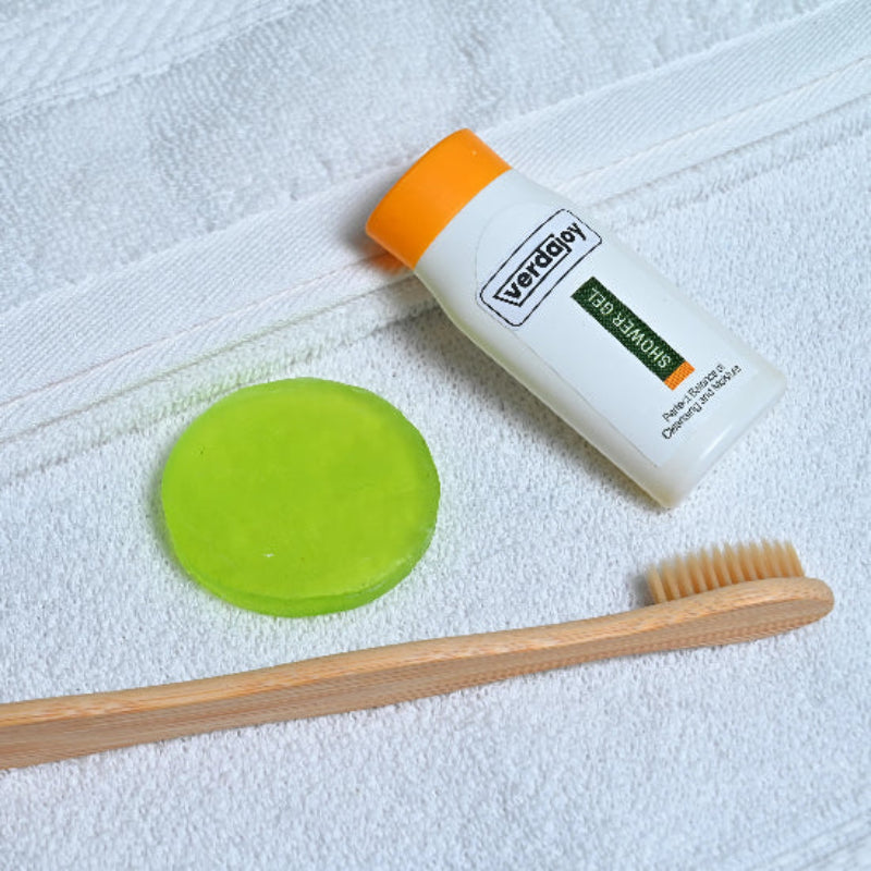 A bamboo toothbrush, bath soap, toothpaste, and a tube of shower gel product on a white cotton towel.