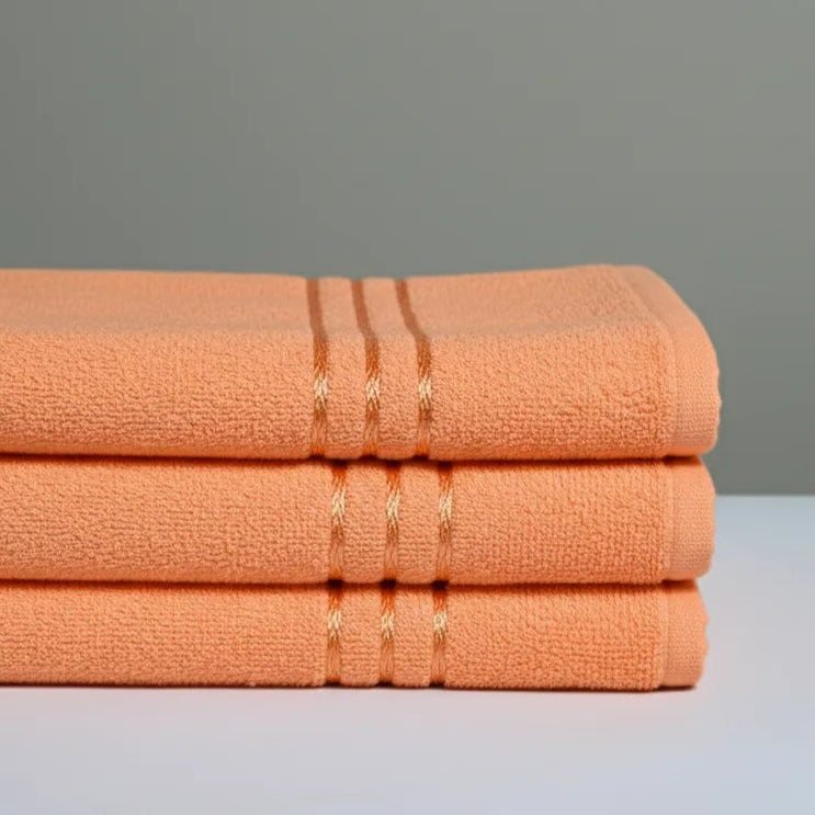 Stack of three folded peach-colored towels on a light gray surface with a neutral gray background