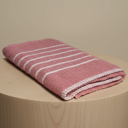 Folded pink towel with white stripes on a wooden stool against a beige background