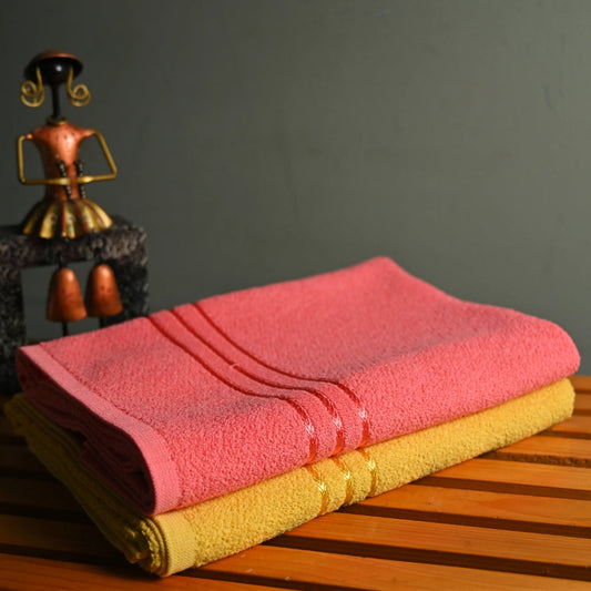 Pink and yellow folded bath towels on a wooden surface with a dark background.