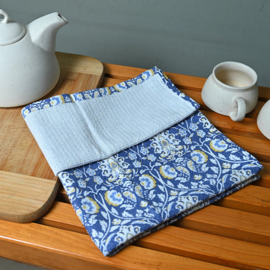 Tea set with a teapot, cups, and a folded blue and white patterned cloth on a wooden surface.