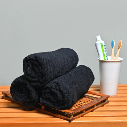Two black towels on a wooden tray with a cup containing toothbrushes and toothpaste on a gray background.