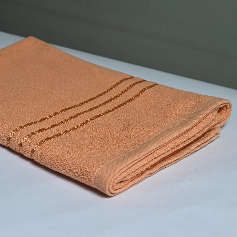 a bath towel, saffron color placed on a white table with grey background.