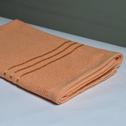 a bath towel, saffron color placed on a white table with grey background.