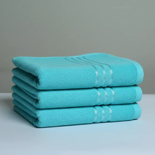 Stack of three turquoise towels on a light gray surface with a neutral background