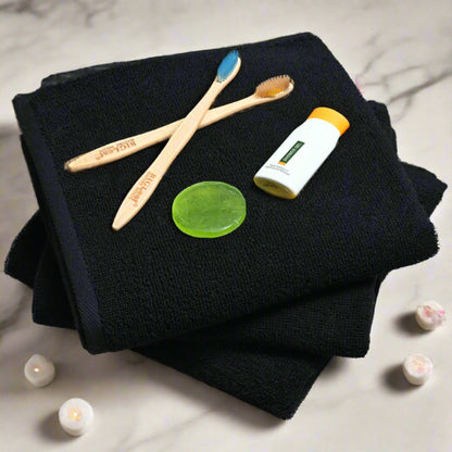 Two bamboo toothbrushes, a bottle of mouthwash, and a green bath soap on a black towel with rose candles around.