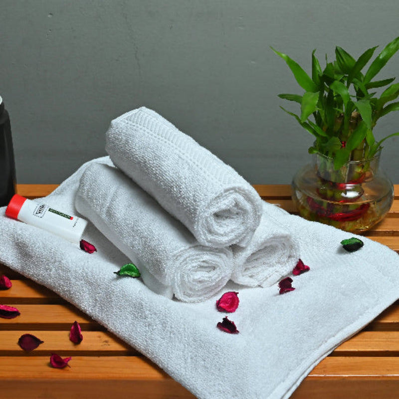 Three rolled-up towels on a white towel with a black mug and plant on a wooden surface.