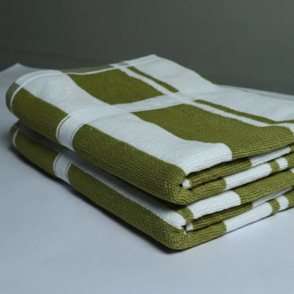 Stack of green and white striped towels on a white surface with a gray background