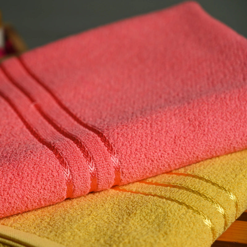 Pink and yellow bath towels on a wooden surface with blurred jars in the background.